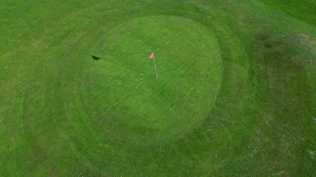 Top down overview of golf green and sand bunker with lawn cut fresh around flag