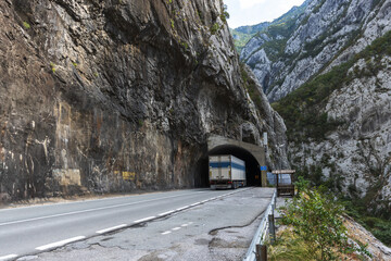 Fototapeta premium A large truck nears a dark tunnel, mountain road view