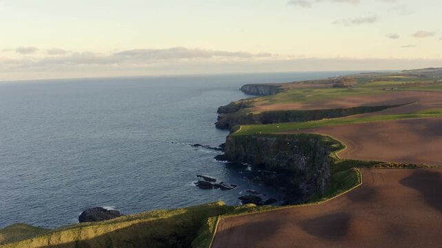 Aerial view of the rugged Stonehaven coastline with dramatic cliffs meeting the North Sea, showcasing a blend of green fields and brown earth, Stonehaven, Scotland, United Kingdom.