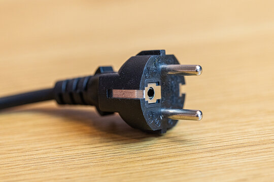 Electric plug on a wooden table with natural grain texture. Close-up of a power connector resting on a rustic wooden surface, ideal for technology, electronics, home office, energy, and workspace conc