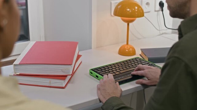 Cropped shot of unrecognizable blind man sitting at desk with stack of books and learning how to use computer keyboard with braille display