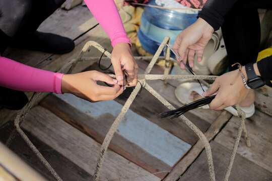 Close-up view of hands attaching black cable ties to a spider-shaped metal rebar frame, preparing it for live coral fragments as part of a tropical reef restoration and Marine conservation project