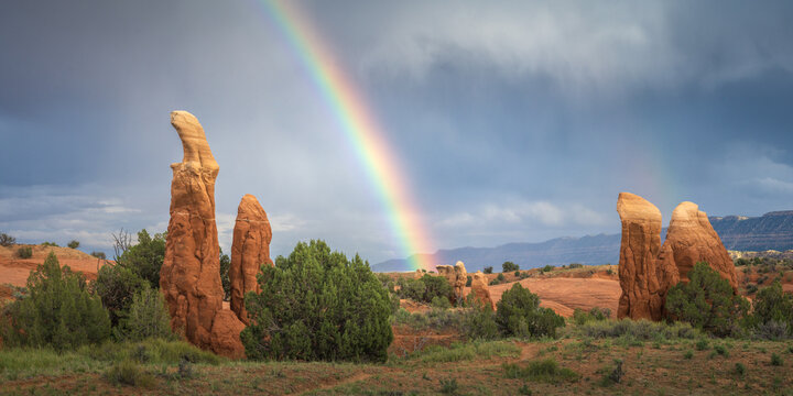 View of vibrant rainbow arcs across the sky, illuminating the textured sandstone formations and green vegetation in a striking contrast, Escalante, Utah, United States.