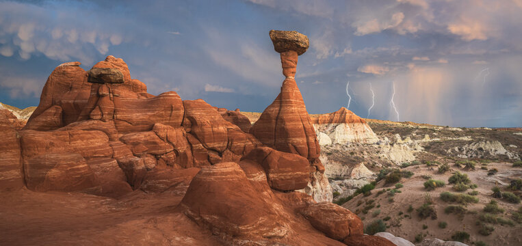 View of striking rock formations bathed in warm light, juxtaposed against a stormy sky with lightning illuminating the distant landscape, Escalante, Utah, United States.