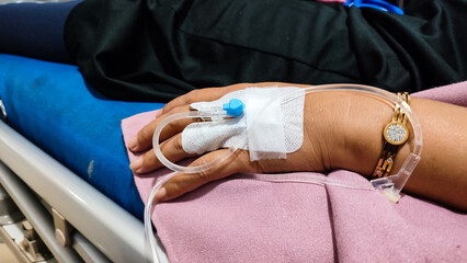 A close-up view of a patient&rsquo;s hand resting on a pink hospital blanket, fitted with an intravenous (IV) catheter secured by medical tape, symbolizing healthcare, recovery, and medical treatment.