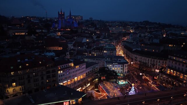 Aerial view of the illuminated Lausanne Cathedral towers over the city's Christmas market, creating a festive glow, Lausanne, Vaud, Switzerland.