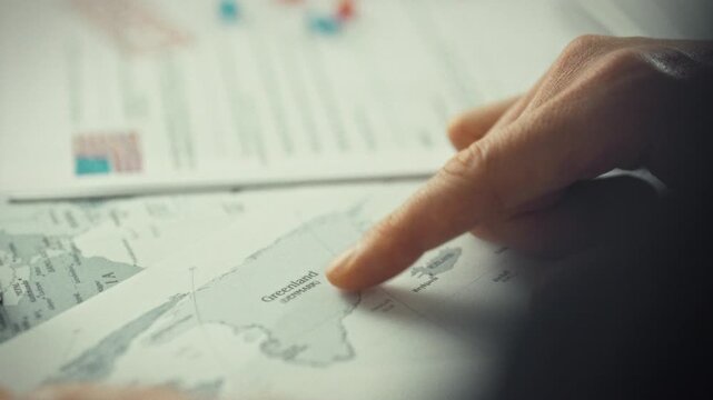 Government representative points to Greenland on vast map surrounded by documents, highlighting island's autonomy within the Kingdom of Denmark, situated between the Arctic and North Atlantic Ocean