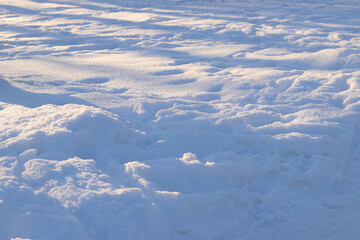 Deep snow at sunset. The meadow is covered with white snow. Footprints in the snow, snowdrifts. Winter landscape. Winter snow background, side view with selective focus