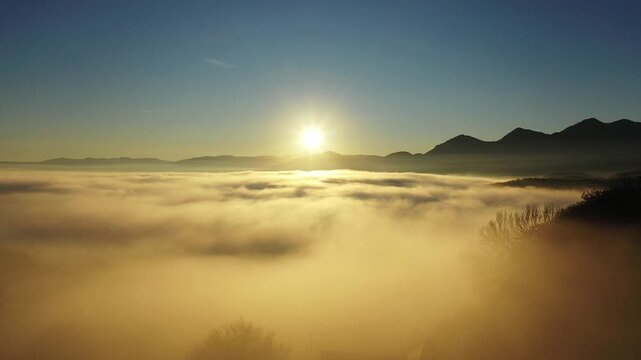 Aerial view of a golden sea of clouds blanketing the landscape, with mountain peaks piercing through, bathed in the warm glow of the rising sun, Brasov, Brasov, Romania.