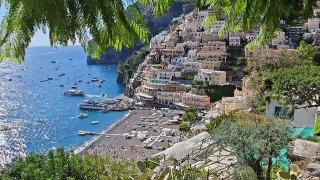 Amalfi Coast, Italy. Scenic coastal view of Positano, Italy, showcasing vibrant buildings on cliffs, sandy beach, and boats anchored in the turquoise waters under bright sunlight