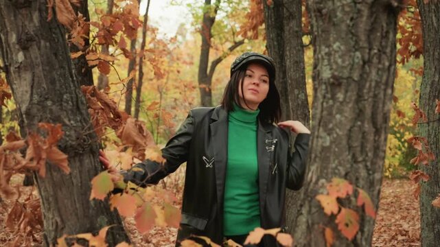woman in leather jacket amid autumn oaks, confident model explores woodland, green turtleneck and cap, leaves rustle around trunk, candid portrait with rugged vibe and cinematic composition