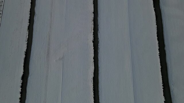 Aerial view of the stark white snow blankets the fields dissected by dark canals, creating a serene winter landscape, Delft, South Holland, Netherlands.