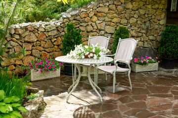 White petunias in pots on a table in the summer garden.  Metal garden table and chairs