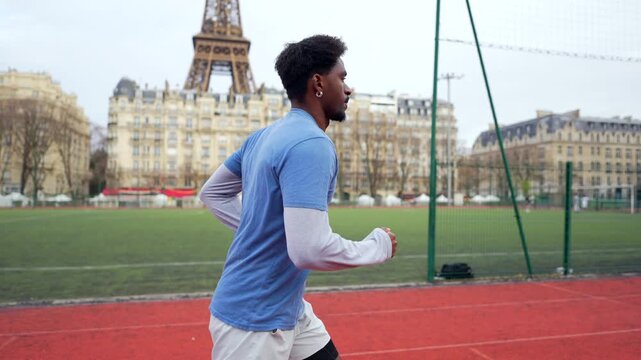 Young athletic man training with purpose and determination on a red running track in an urban stadium, with the iconic eiffel tower and parisian buildings visible in the background