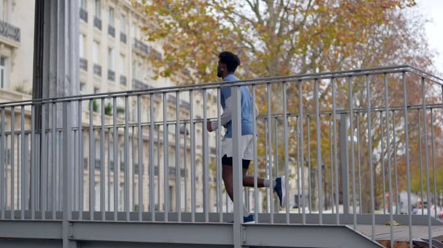 Determined african american athlete enjoying his morning jogging session, running up the stairs and crossing a bridge in paris, france, for a high intensity interval training cardio workout