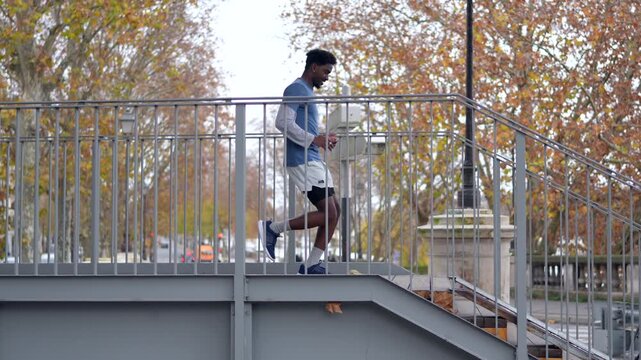 Young athletic black man running across a modern metal footbridge in paris, france, as part of his daily fitness routine, demonstrating a healthy and active urban lifestyle during autumn