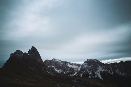 View of jagged peaks pierce the sky, their rocky faces kissed by snow, as shadows dance across the rugged terrain, Urtijei, Trentino-South Tyrol, Italy.