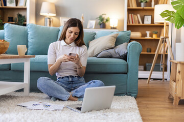 Obraz premium Phone call, laptop and coffee with a black woman lying on the floor of her home living room alone. Computer, mobile and drink with a female browsing online in her house over the weekend to relax.