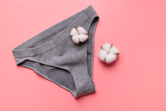 Women's gray ribbed panties with cotton flowers on pink background, flat lay top view. Comfortable cotton panties for girls. Modern female underwear. Comfortable, stylish clothing for hygiene 