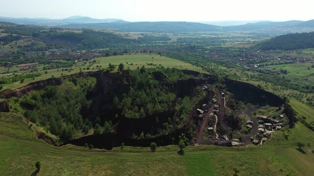 Aerial view of the Racos Volcano, a dramatic landscape where dark volcanic rock meets green vegetation, Racos, Judetul Brasov, Romania.