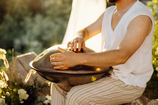 Close-up of hands playing a handpan drum in warm sunlight, capturing rhythm, movement and a peaceful outdoor music experience.