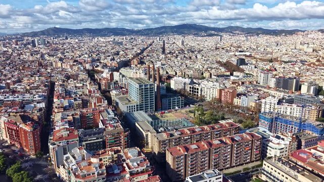 Aerial drone flight over the dense urban grid of the Sant Antoni neighborhood in Barcelona, showing residential buildings, streets, and the cityscape extending to the hills, Spain