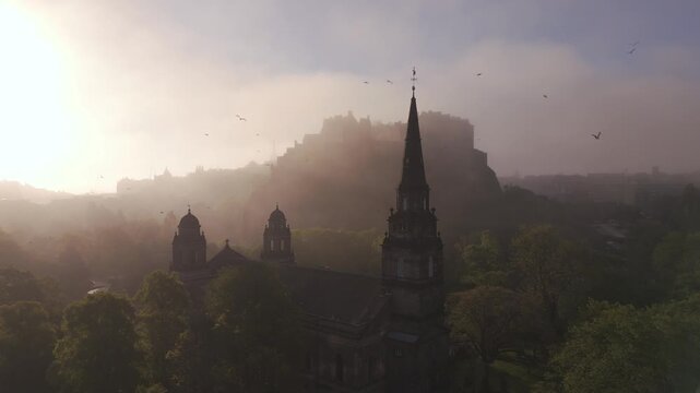 Aerial view of Edinburgh Castle and a church steeple piercing through the mist, creating a serene yet dramatic scene, Edinburgh, United Kingdom.