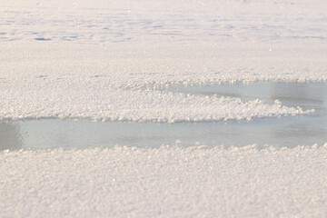 Frozen river covered with ice and snow, side view with selective focus. Snow sparkles in the sun. Frozen surface of a river or lake covered with snow, sparkling snow crystals. Winter landscape