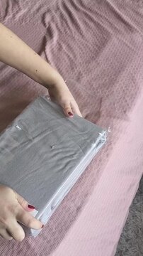 Female hands unpack a sheet with an elastic band. A woman takes new bedding out of the package on the background of the bed in the room.