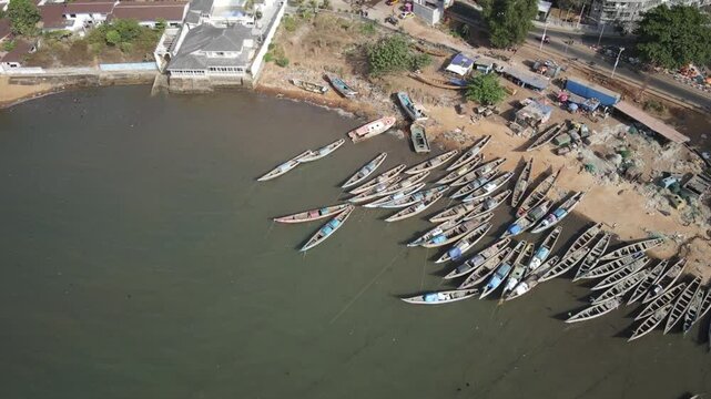 Aerial view of fishing boats lined up on the shore, the serene water reflecting the sky, a vibrant contrast to the sandy coastline, Freetown, Sierra Leone.