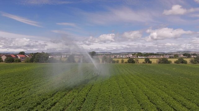 Aerial view of farmland being irrigated with a sprinkler system, creating a vibrant rainbow, contrasting with the green fields, Cupar, Scotland, United Kingdom.