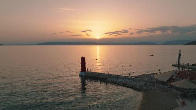 Aerial view of the red lighthouse standing tall on a pier as the sun sets over the calm sea in Cres, Primorsko-goranska zupanija, Croatia.