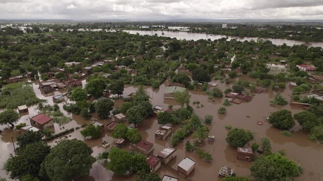 Aerial view of homes submerged in muddy floodwater, with only rooftops and trees visible, creating a stark contrast against the overcast sky, Boane, Maputo Province, Mozambique.