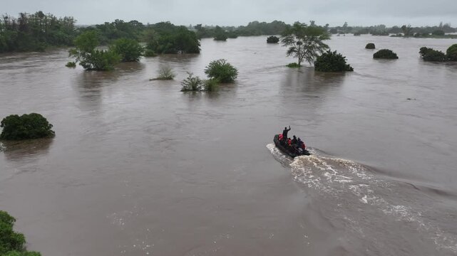 Aerial view of a boat navigating through a flooded river surrounded by lush green trees and murky waters, Boane, Maputo Province, Mozambique.