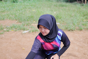 Young Asian woman volleyball player wearing hijab stretches her body to warm up before practice on an outdoor volleyball court in rural village. Pre-training routine, grassroots, and active lifestyle