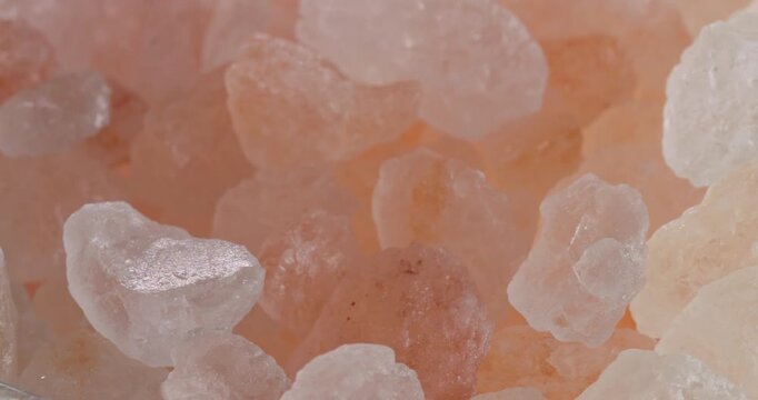 Pink Himalayan Salt Crystals Seamless Loop. Close-up macro view of coarse rose-colored Himalayan salt grains gently sparkling under soft lighting.