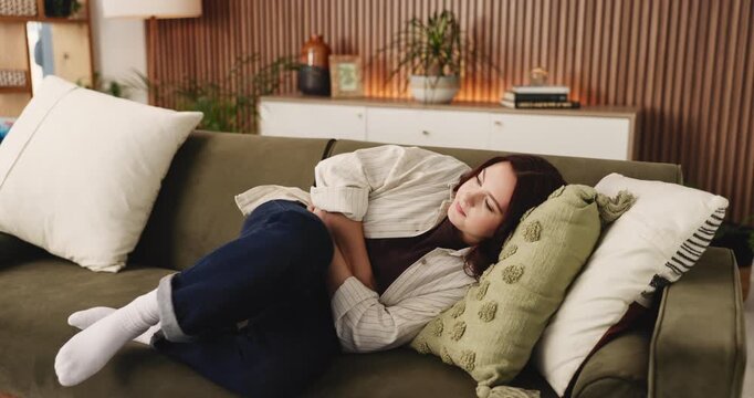 Woman, stomach ache and sofa with pain for menstruation, indigestion or gastrointestinal reflux. Female person, lying and belly with sore cramp for constipation, tummy bug or virus on couch in home