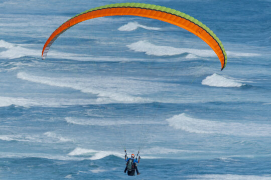 View of a paraglider soars over the turbulent ocean, a vibrant splash of color against the blue and white waves, Wilderness, Western Cape, South Africa.