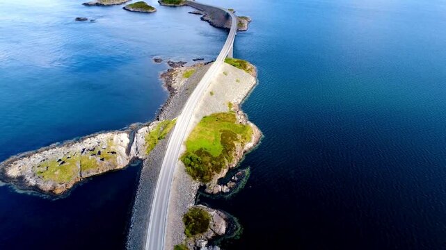 aerial drone shot captures the iconic Atlantic Ocean Road bridge in Norway during winter, with the road and surrounding islets covered in pristine snow, contrasting beautifully with the dee
