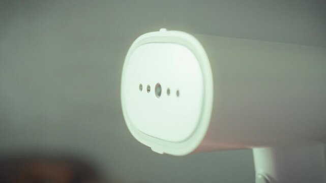 The clothes sender is operation, emitting hot steam from its heating element, releasing vapor, indicating preparation process for sending or smoothing out wrinkled clothing, leveraging iron-like heat