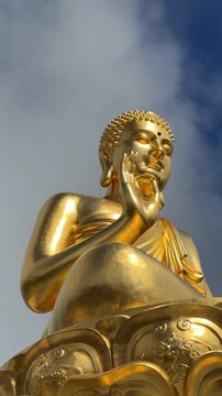 Vertical view of a golden Buddha statue with Vitarka mudra as a Buddhist flag waves beside it, set against an overcast sky that enhances a quiet spiritual mood. Temple devotion.