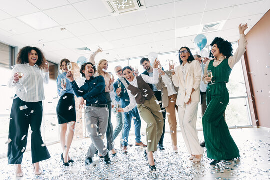 Group of diverse office coworkers celebrating a success together with confetti and champagne in bright workplace setting