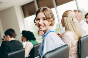 A cheerful woman at a professional business meeting glances, seated with colleagues in a conference...