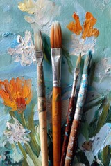 Education training class. Knowledge learning improvement study. A closeup of paintbrushes with vibrant orange and white flowers painted on a canvas. The background is a blend of blue and green.
