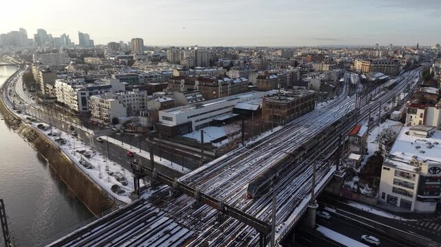 Aerial drone viewof extensive railway tracks and train yards with urban buildings along Seine River during winter morning light, Paris, France