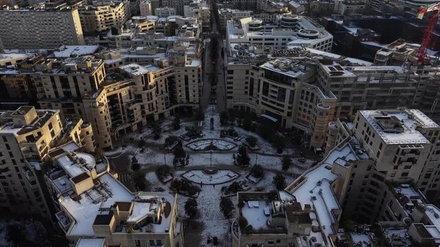 Top-down aerial view of elegant snow-covered circular courtyard surrounded by residential buildings with symmetrical design in Paris, France