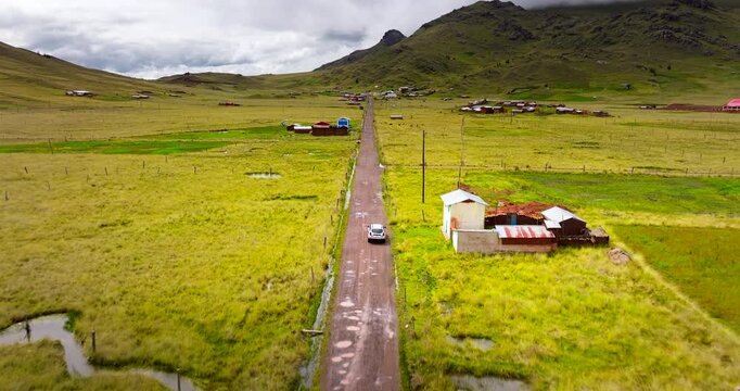 Car on off the beaten path road trip through lush farm fields in Peru, aerial