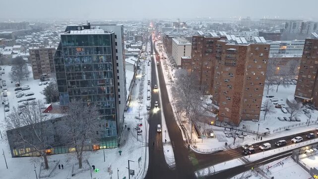 Cinematic aerial view of snow-covered street with modern residential buildings and winter traffic in urban Parisian neighborhood, France