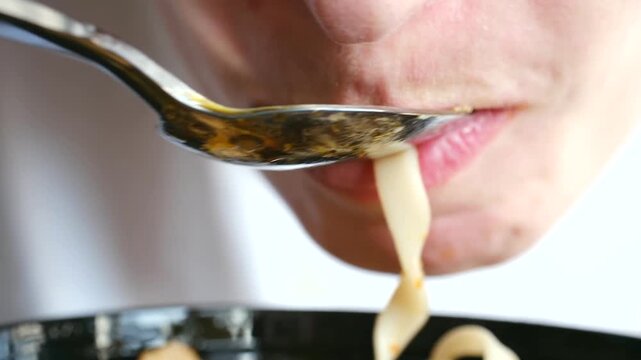 Extreme close up person mouth eating hot asian soup with noodles, mushrooms, wakame seaweed using spoon, showing enjoyment traditional oriental meal in restaurant. Person eating delicious asian soup