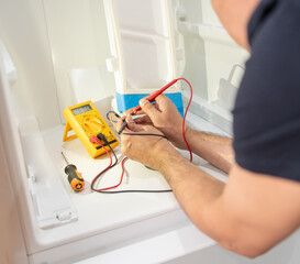 Close-up on an electrician fixing an electrical outlet of refrigerator and measuring the voltage.